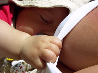 Vier Monate alter Junge (Baby) schl&auml;ft im Tragetuch und h&auml;lt sich an Mamas Bluse fest