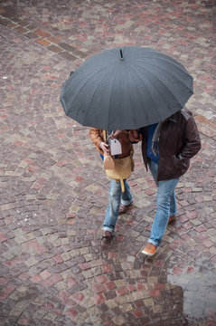 couple marchant avec un parapluie sur un place pavée