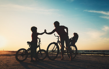 Obraz na płótnie Canvas happy mother with kids biking at sunset