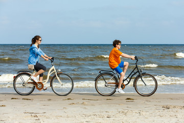 Naklejka premium Teenage girl and boy biking on beach