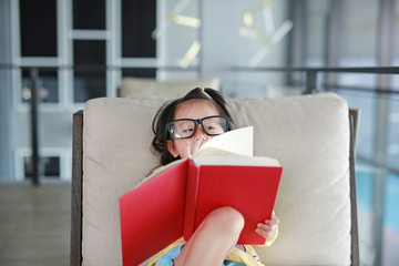 Little child girl with Glasses reading book in library, Education concept.
