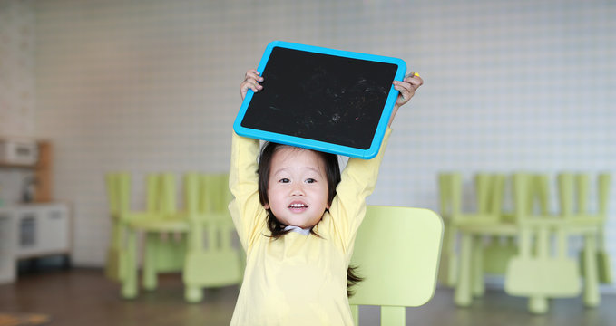 Cute asian child girl holding empty blackboard in playroom.