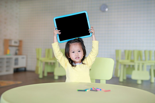 Cute asian child girl holding empty blackboard in kids room.