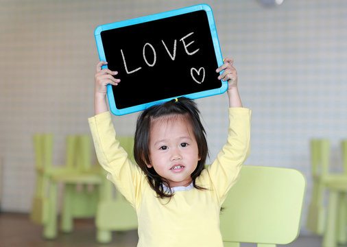 Cute little child girl holding blackboard showing text " LOVE " in kids room. Education concept.