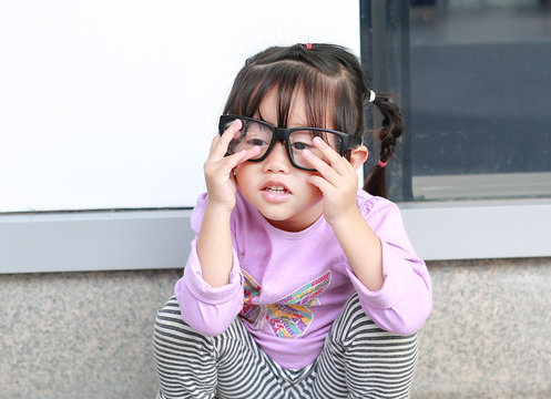 Portrait of cute little girl trying to wear glasses.