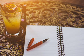 pen and fruit juice on the desk, open a blank white notebook on table