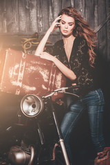 Fototapeta na wymiar Pretty biker girl standing with vintage suitcase at motorcycle