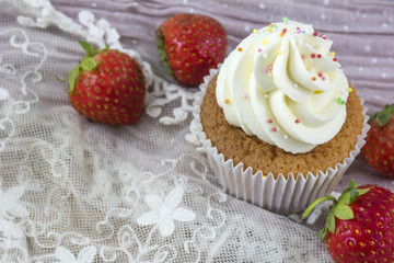 One vanilla cupcake with white cream and several strawberries on the pink lace background