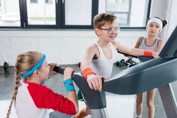 funny kids in sportswear training on treadmill at gym together, children sport concept
