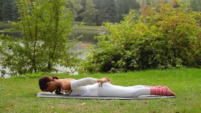Young woman does yoga asana while lying on her stomack at a river bank