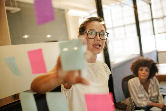 Businesswoman pointing at sticky note to colleague