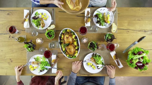 Overhead top view table four caucasian friends eating lunch, drinking, toast together with chicken,sala, potatoes, red wine. in modern house home. 4k video
