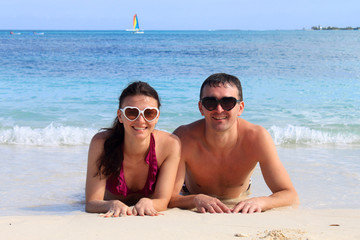 Fototapeta premium Happy couple wearing sunglasses lying on the beach at Bahamas