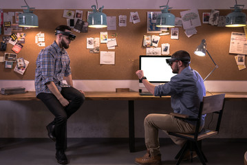 Two young adult Caucasian males discussing a project using holographic augmented reality glasses in...