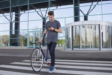  Man with a fixie bicycle walking on the road. young hipster with retro bicycle walking on the crosswalk and texting on the cellphone