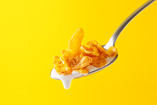 Corn flakes with milk on a spoon on a yellow background. Macro. Focused. Close-up