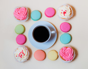 White coffee cup with colorful macaroons and cupcakes on beige background