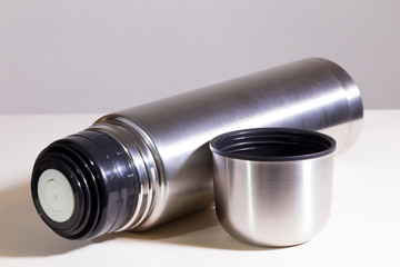 Metal vacuum flask.
Closeup of a stainless steel vacuum flask and its cup on white surface.
