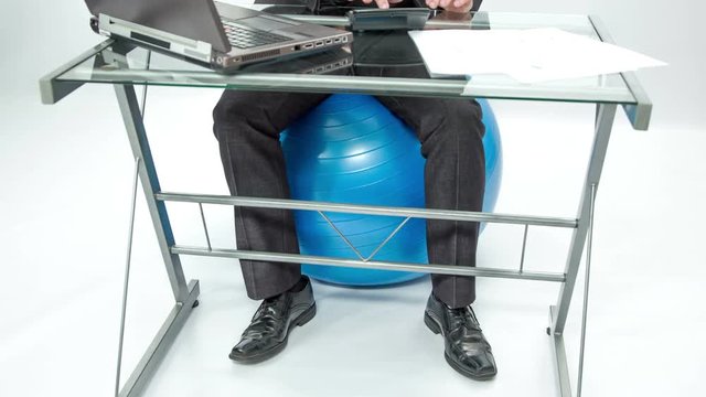A young man is sitting on the exercise ball and he is working and moving his lower body. He is having a good time.