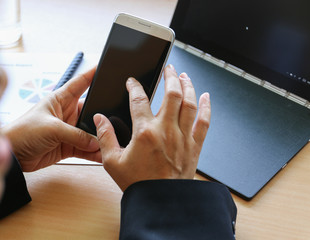 hands holding smart phone before laptop and pen on wood desk background