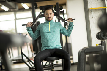 Young man doing exercise for triceps in the gym on mashine