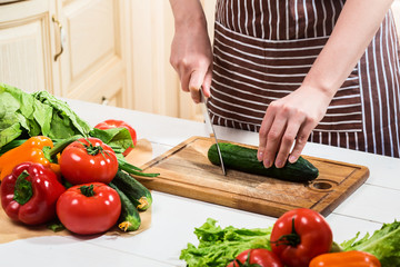 Young woman cooking in the kitchen at home. A woman cuts a cucumber and vegetables with a knife.