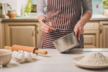 Young woman holding bowl with dough and whisk, closeup