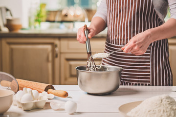 Young woman holding bowl with dough and whisk, closeup