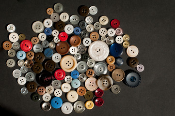 Colorful mix of clothing buttons, various sizes, spilled out on black background