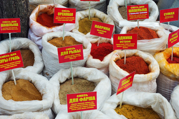 Large selection of spices packaged in bags and sold on market in open air. The names of spices are listed in Russian. Selling spices. Sell by weight.