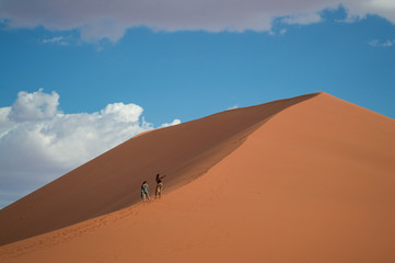 Fototapeta na wymiar Two Women Walking up Dune 45, Desert Landscape, Sossusvlei, Namibia