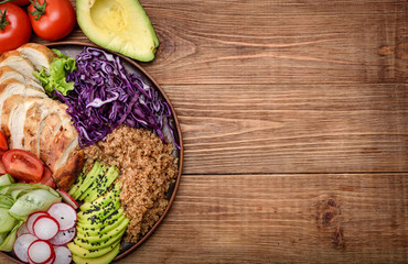 Healthy salad bowl with quinoa, chicken, avocado and vegetables on wooden background .
