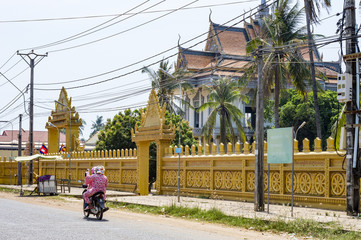 Street view in Cambodia - two women driving motorbike on the street near Buddhist temple in Kratie, Cambodia