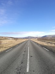 Driving on an empty open asphalt road towards a range of mountains covered in snow on blue sky sunny day, symbolizing business success and way forward, Road trip travel in iceland, journey path