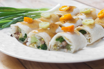 Fresh spring rolls and vegetables eaten on wooden table.