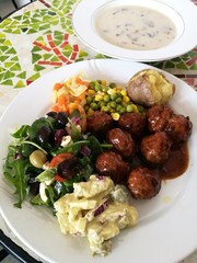 Meatballs spicy sweet and sour tomato sauce with fresh vegetable, potato salad and soft boiled cabbage carrot,corn and bean on white plate,foreground focused and blur mushroom soup bowl background
