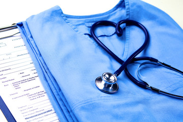 Medical stethoscope twisted in heart shape lying on patient medical history list and blue doctor uniform closeup