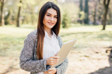 Fototapeta premium Young woman walking in the park with laptop in hands