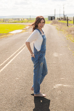 Pretty woman wearing overalls outside near a country field