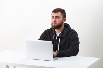 The programmer with glasses works behind the laptop. Isolated, one person on a white background. He is calm.