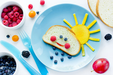 Creative breakfast idea for kids - bread bun with fruit and berry shaped funny cloud with peach sun and blueberry rain