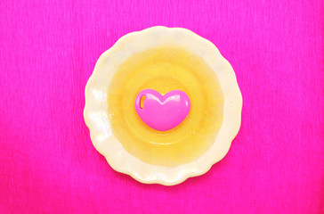 Honey in a saucer is isolated on a pink background. On honey lies the heart: a symbol of love for honey, bees, beekeepers, pollen. Minimalism