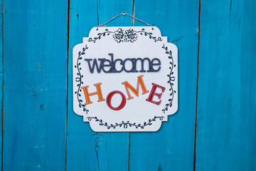 Welcome HOME sign with floral border hanging on rustic antique teal blue wood background