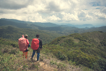Fototapeta na wymiar Two young backpackers enjoying a beautiful view of mountain range. Travel lifestyle