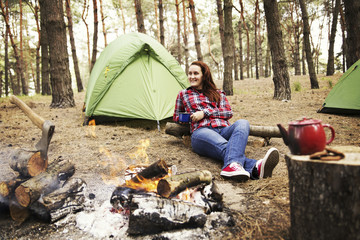 Camping in the forest. The girl sits in a hammock and looks at the fire.
