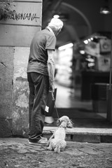 Starszy mężczyzna z psem na smyczy stoi przy wejściu do pasażu handlowego - 151586099