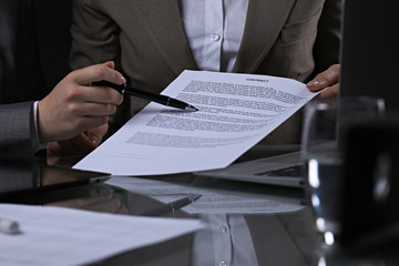 Group of business people and lawyers discussing contract sitting at the table. Woman chief is taking pen for signing papers. Low key lighting