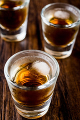 Whiskey Shots with ice on dark wooden surface.