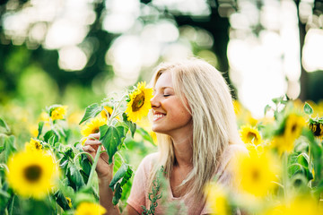 portrait of beautiful young blonde woman smelling sunflower and smiling