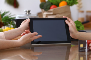 Human hands pointing into touch pad with copy space area. Two woman making menu in the kitchen, closeup. Cooking and friendship concept.